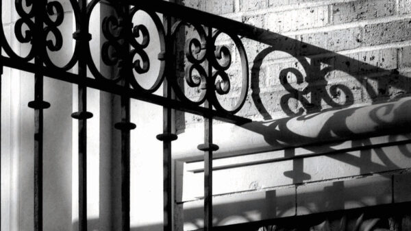 A black-and-white closeup photo of wrought iron gates and a brick wall with some nautilus shell details.