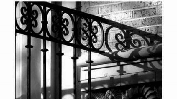 A black and white closeup photo of wrought iron gates and a brick wall with some nautilus shell details.