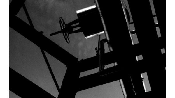 A black and white photo looking up at the chimney stack of a power plant framed by several beams.