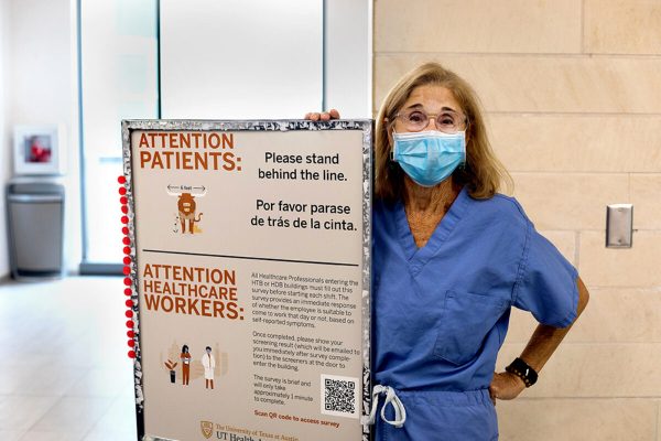 Masked woman in blue scrubs standing behind a sign that says information for patients and healthcare workers