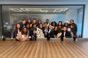 18 women of color standing in two rows behind a large table and smiling