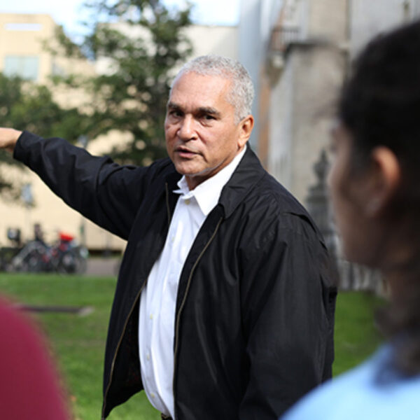 A man in a white shirt and a black jacket pointing off into the distance