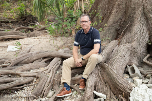 A man sitting on the roots of a large tree.