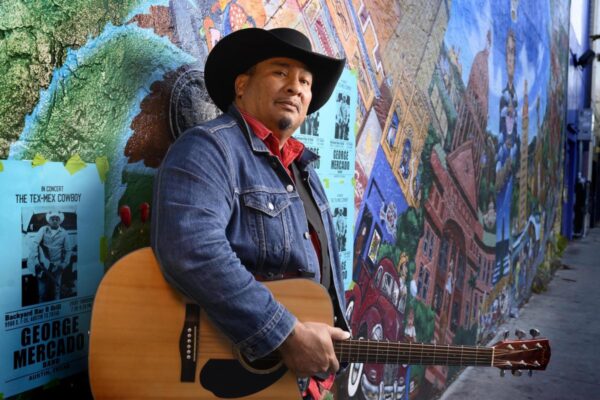 a man holding a guitar and leaning against a mural