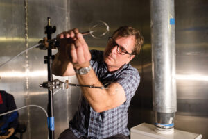 A man with glasses adjust some scientific measuring instruments attached to a rod.