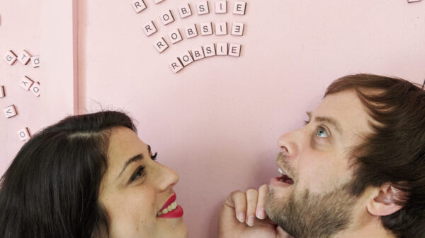 a man and a woman against a pink background staring up at scrabble letters