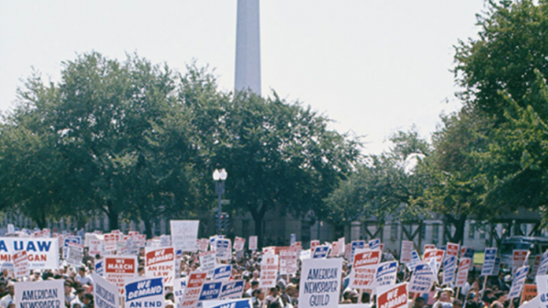 colorized photo of men and women who stand in protests and hold signs up in 1963.