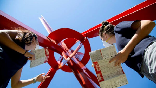 Two girls looking up at a red structure while holding books in their hands