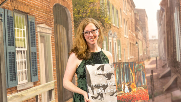 Woman in a green dress holding two art pieces.