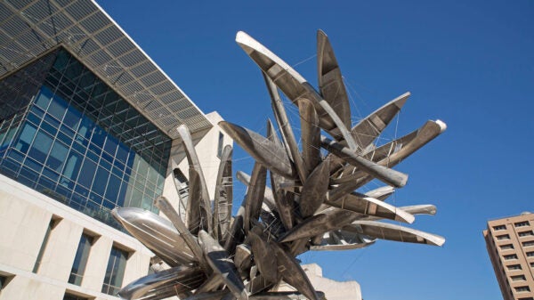 Sculpture consisting of recycled aluminum canoes and small boats clustered at the end of a listing column