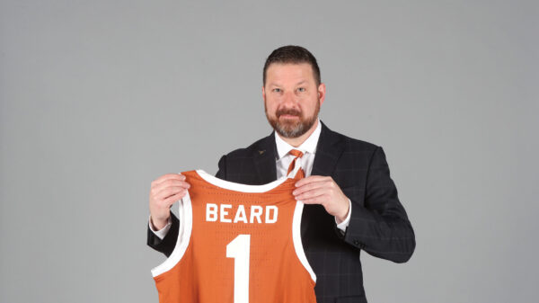 Portrait of Chris Beard holding up a burnt orange basketball jersey that says 