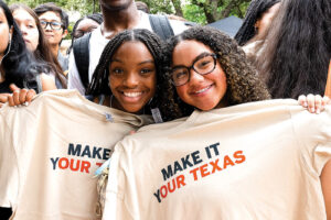 Two students hold Make it Your Texas T-shirts