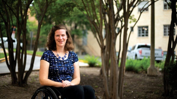 Woman smiles sitting in a wheelchair outside underneath some trees