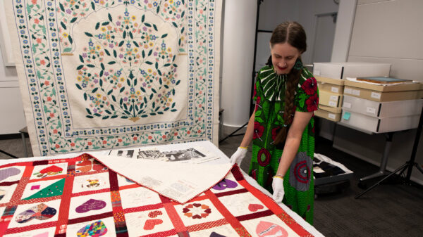 Woman wearing gloves presents a quilt on a table