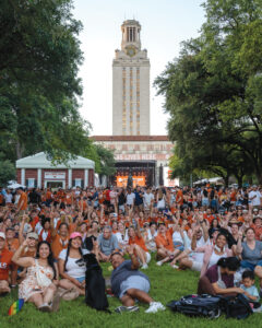 Crowd sitting on the lawn in front of the UT Tower throws up the Hook 'em Horns sign